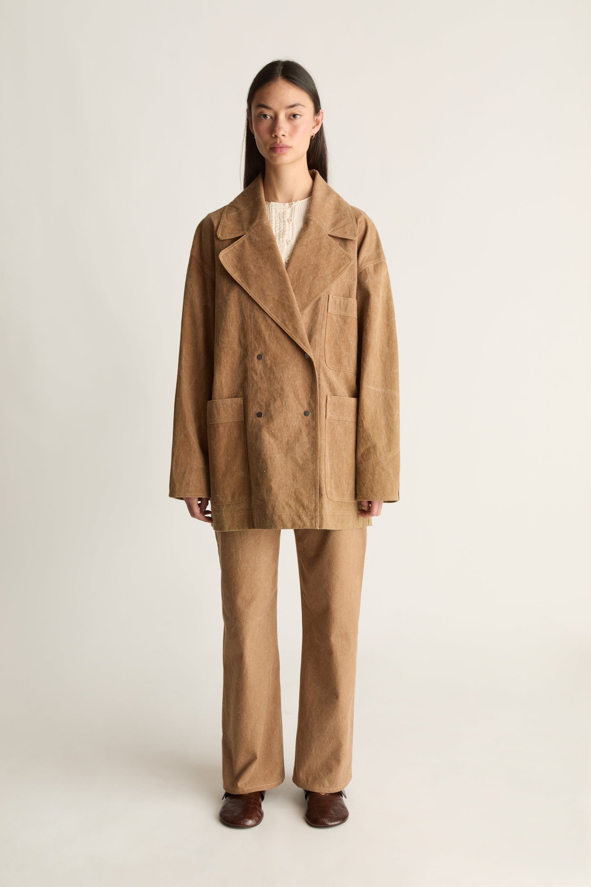 Front view of a woman wearing a brown canvas coat and pants on a white background
