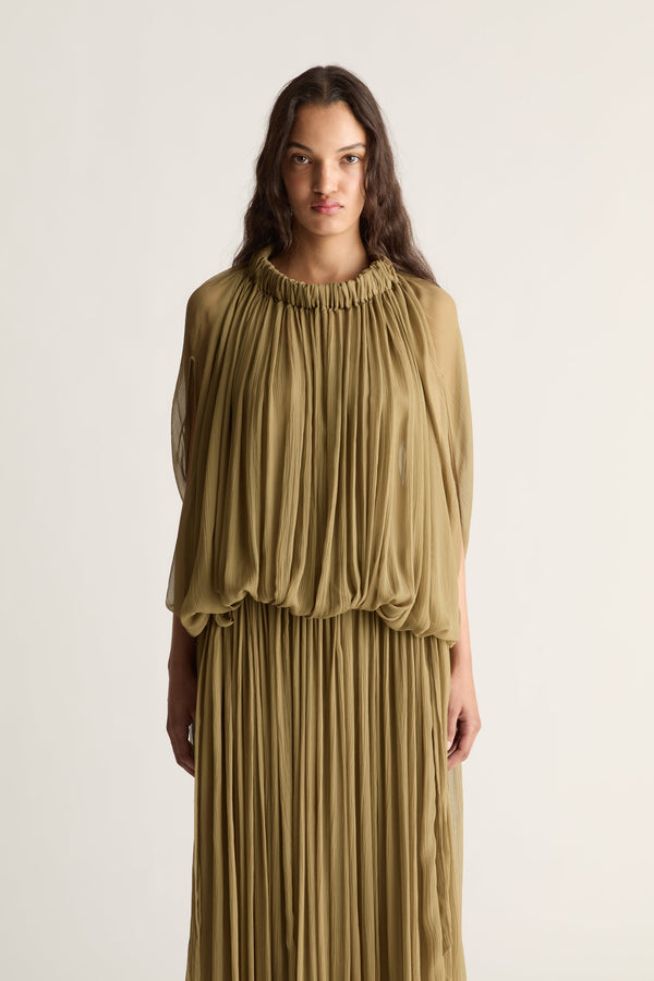 A woman wearing a draped olive green georgette dress set against a plain light background.