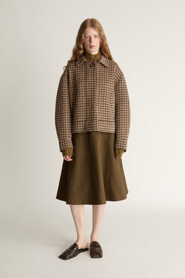 Woman wearing a plaid jacket and brown skirt on a white background