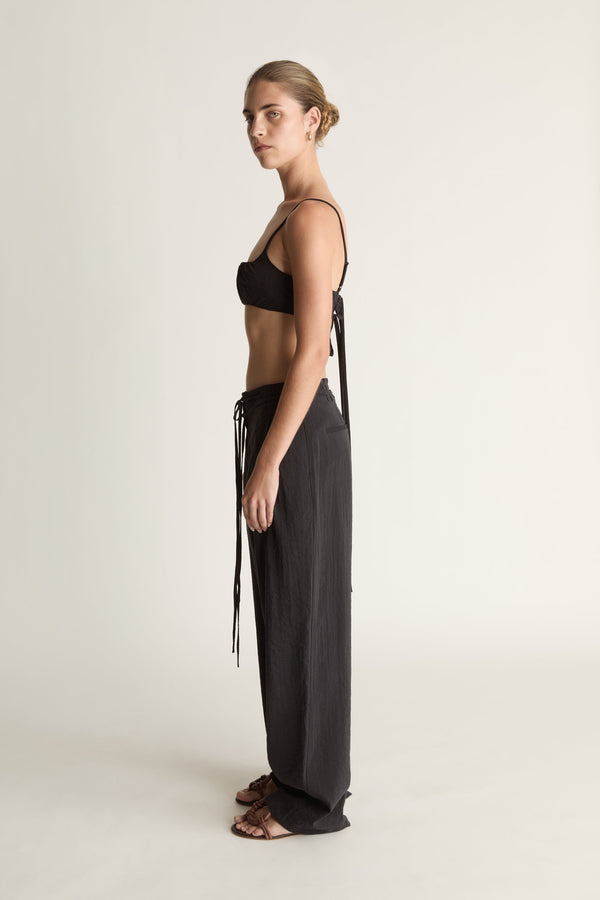 Woman wearing a cropped black top and wide-leg pants on a plain background