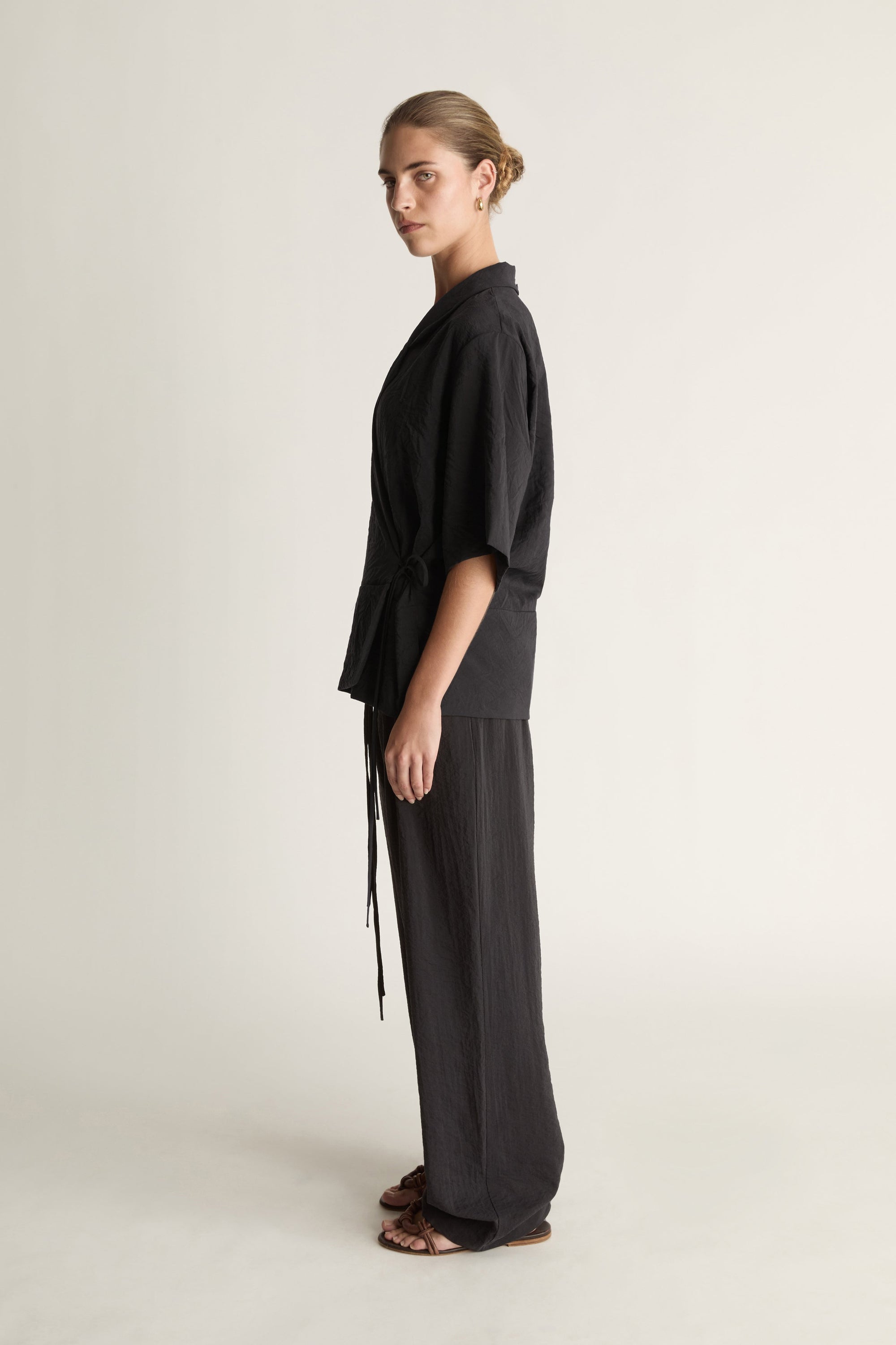 Person wearing a black wrap top with black trousers on a plain background