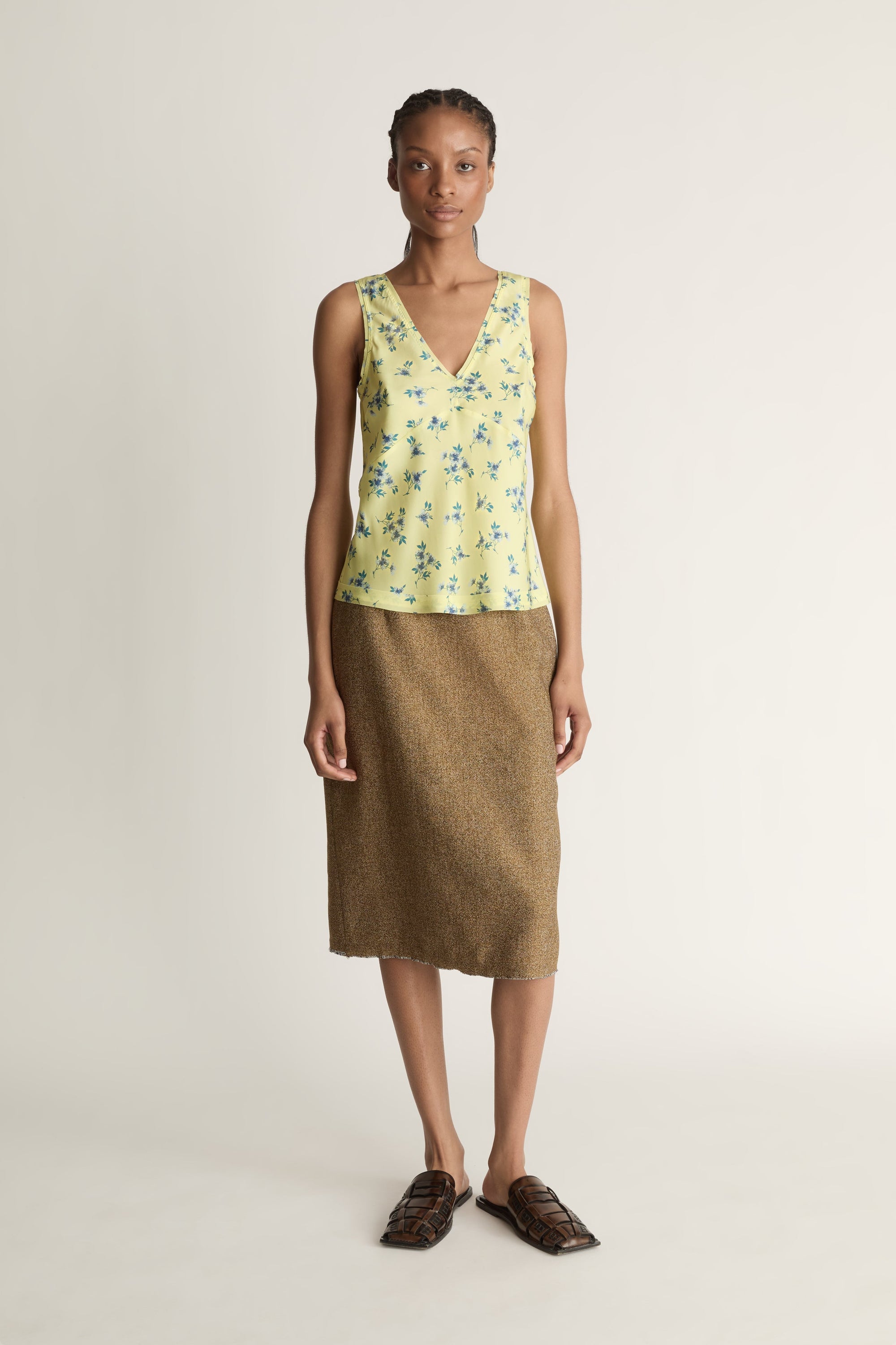 Front view image of a woman wearing a yellow floral sleeveless top and brown skirt on a white background