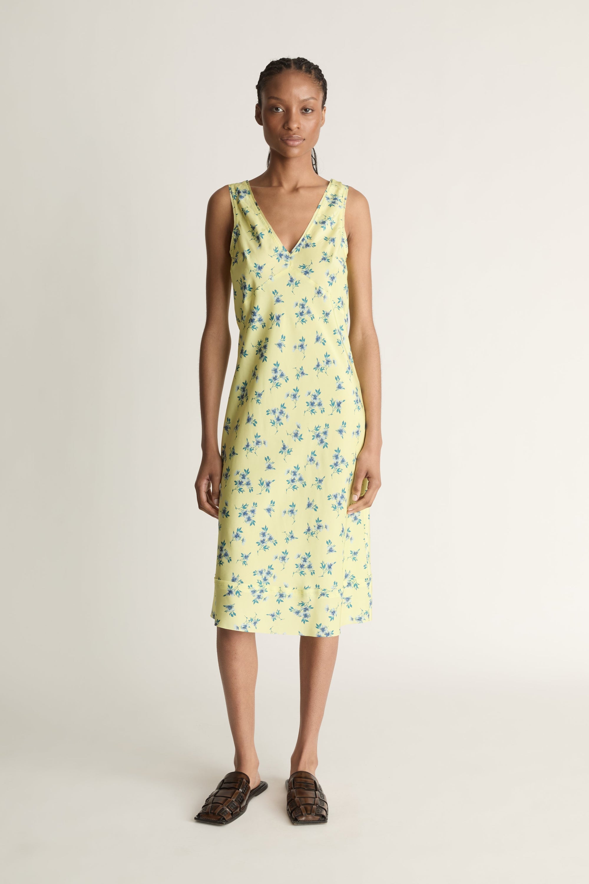 Front view image of a woman wearing a silk slip dress that is a citrus yellow colour with blue flowers on it.
