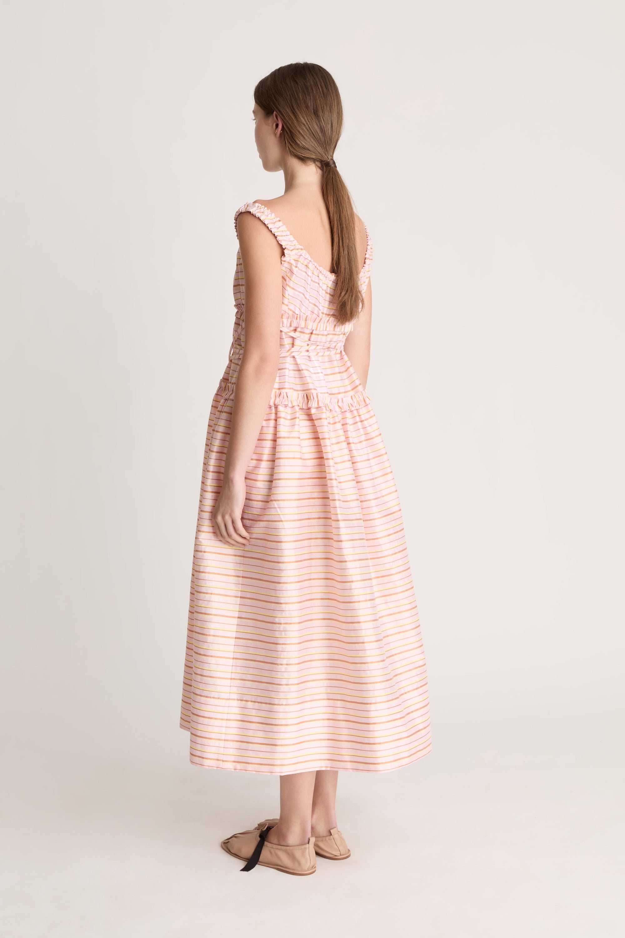 Woman wearing a sleeveless dress with a striped pattern on a plain background
