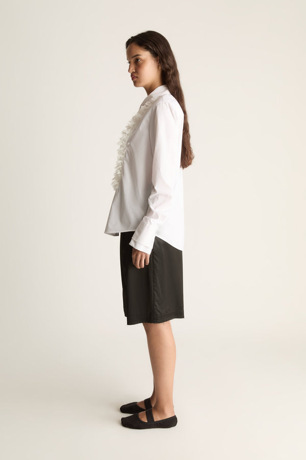 Side view of a woman glancing back in a white button-up shirt with ruffle trim and black shorts