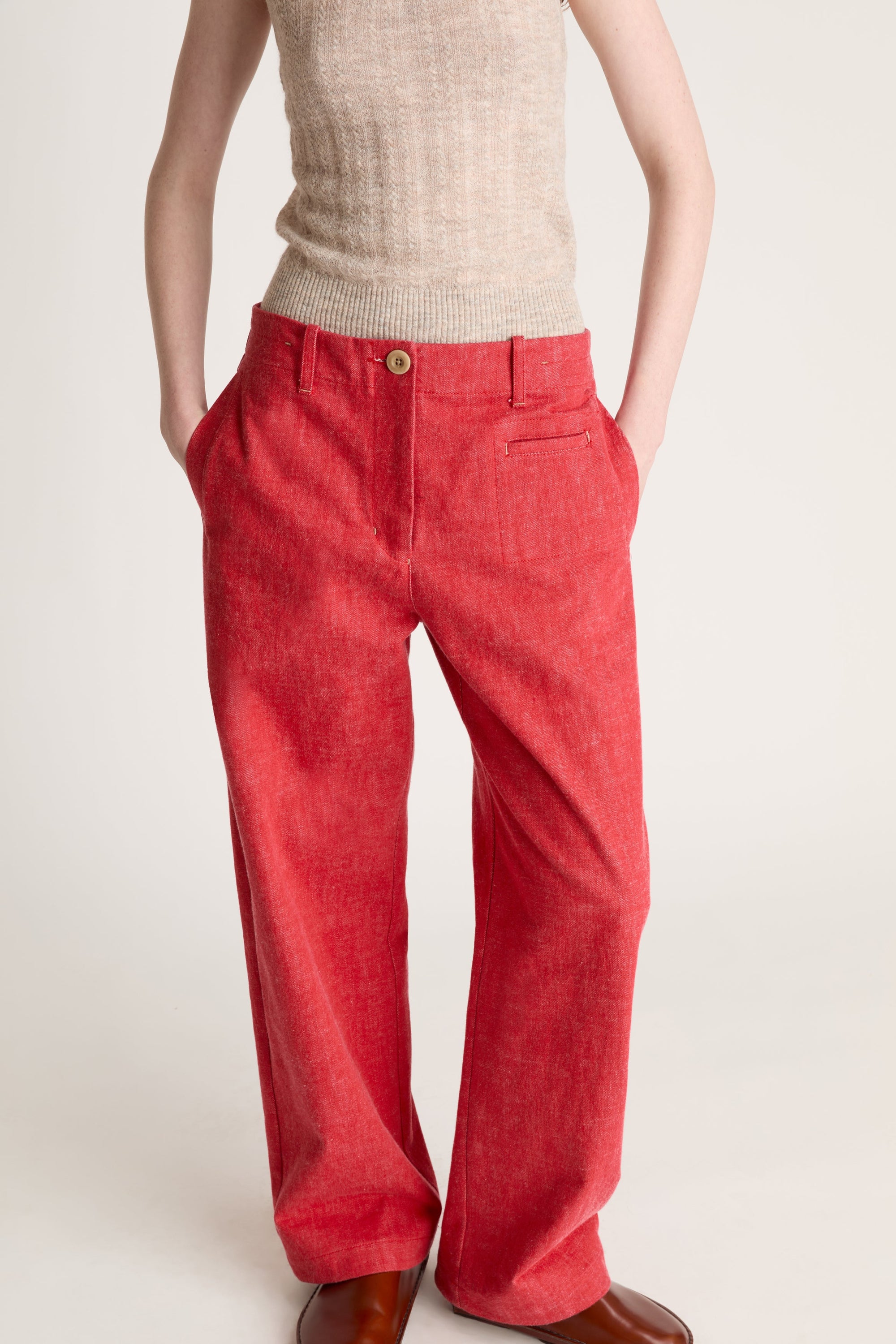 Woman wearing a beige knit cami top and red pants on a white background