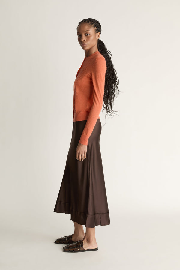 Woman wearing an orange cardigan and brown skirt on a white background