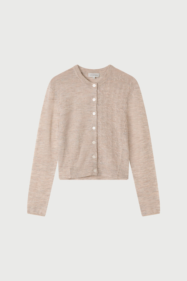 Person wearing a beige cardigan and dark jeans on a white background