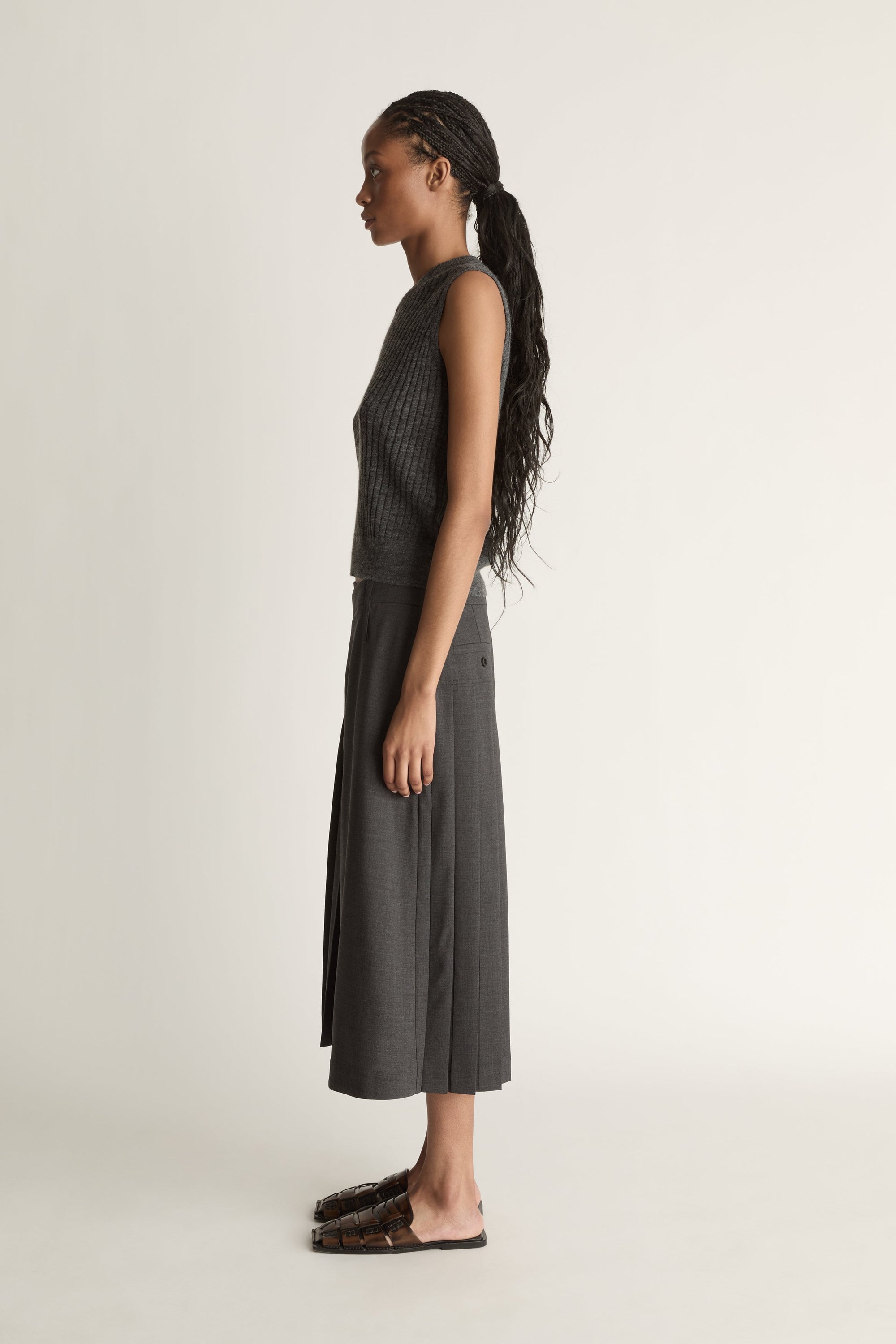 Woman wearing a dark gray sleeveless v neck knit top and skirt on a white background