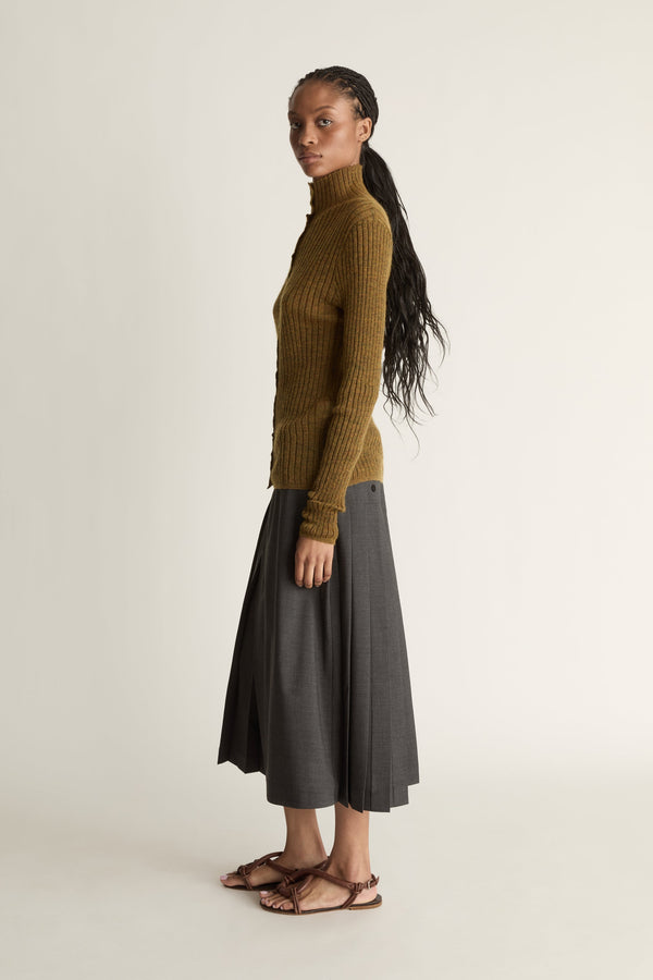 Woman wearing a brown ribbed sweater and gray skirt on a beige background