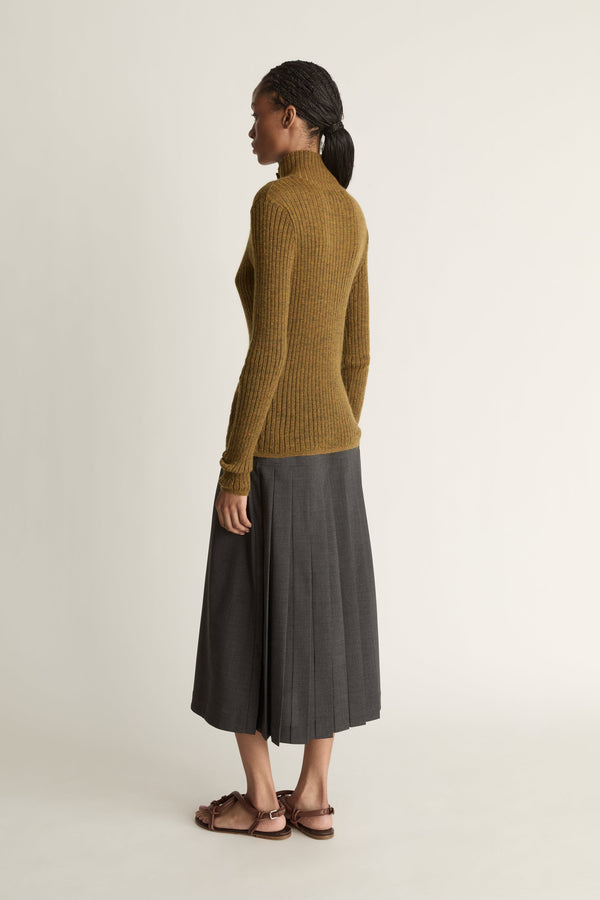 Woman wearing a brown ribbed sweater and gray skirt on a beige background