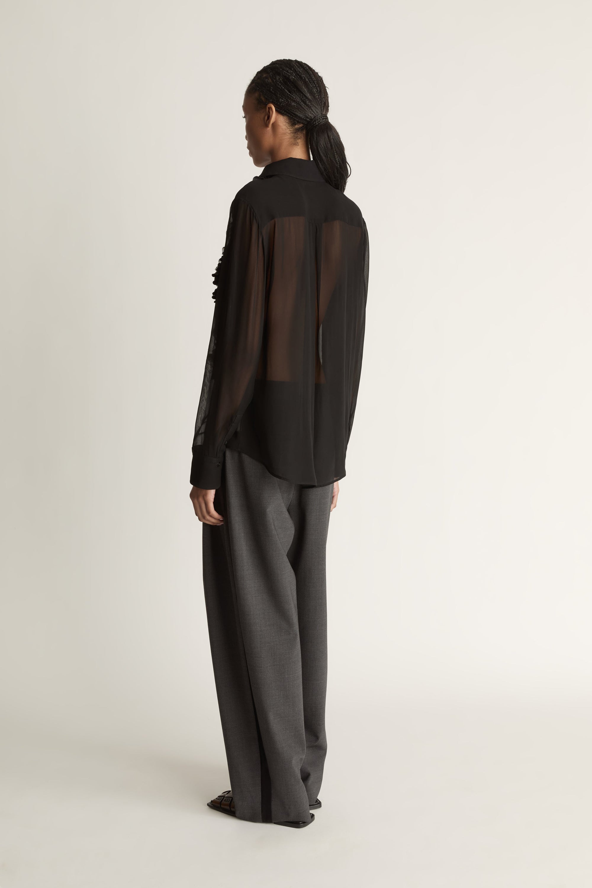 Woman wearing Black sheer shirt and grey trousers on a white background