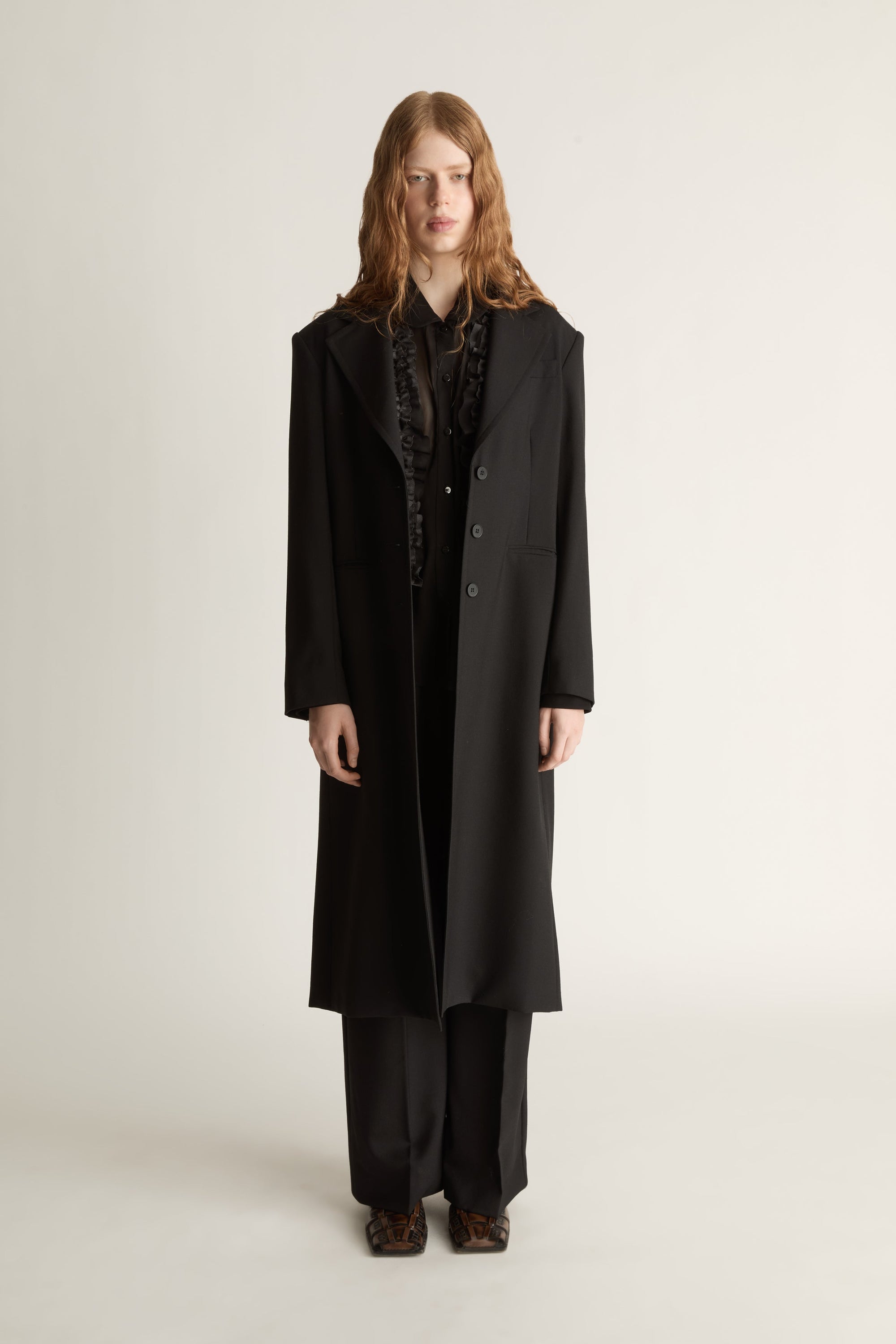 Person wearing a long black coat on a plain background