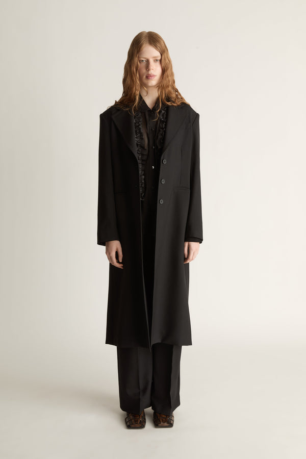 Person wearing a long black coat on a plain background