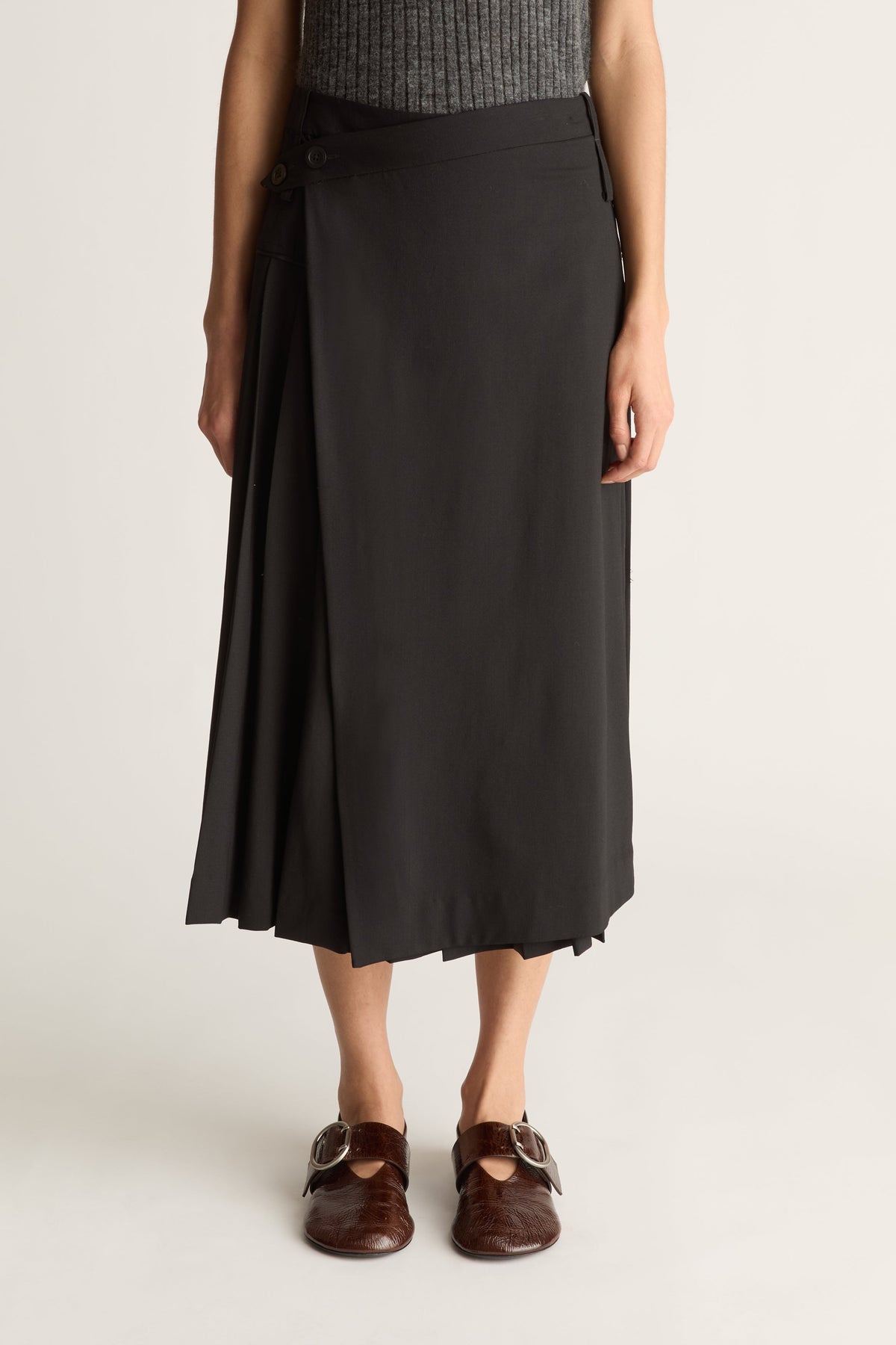 Close-up of a person wearing a black skirt and a grey knit tank against a white studio background.
