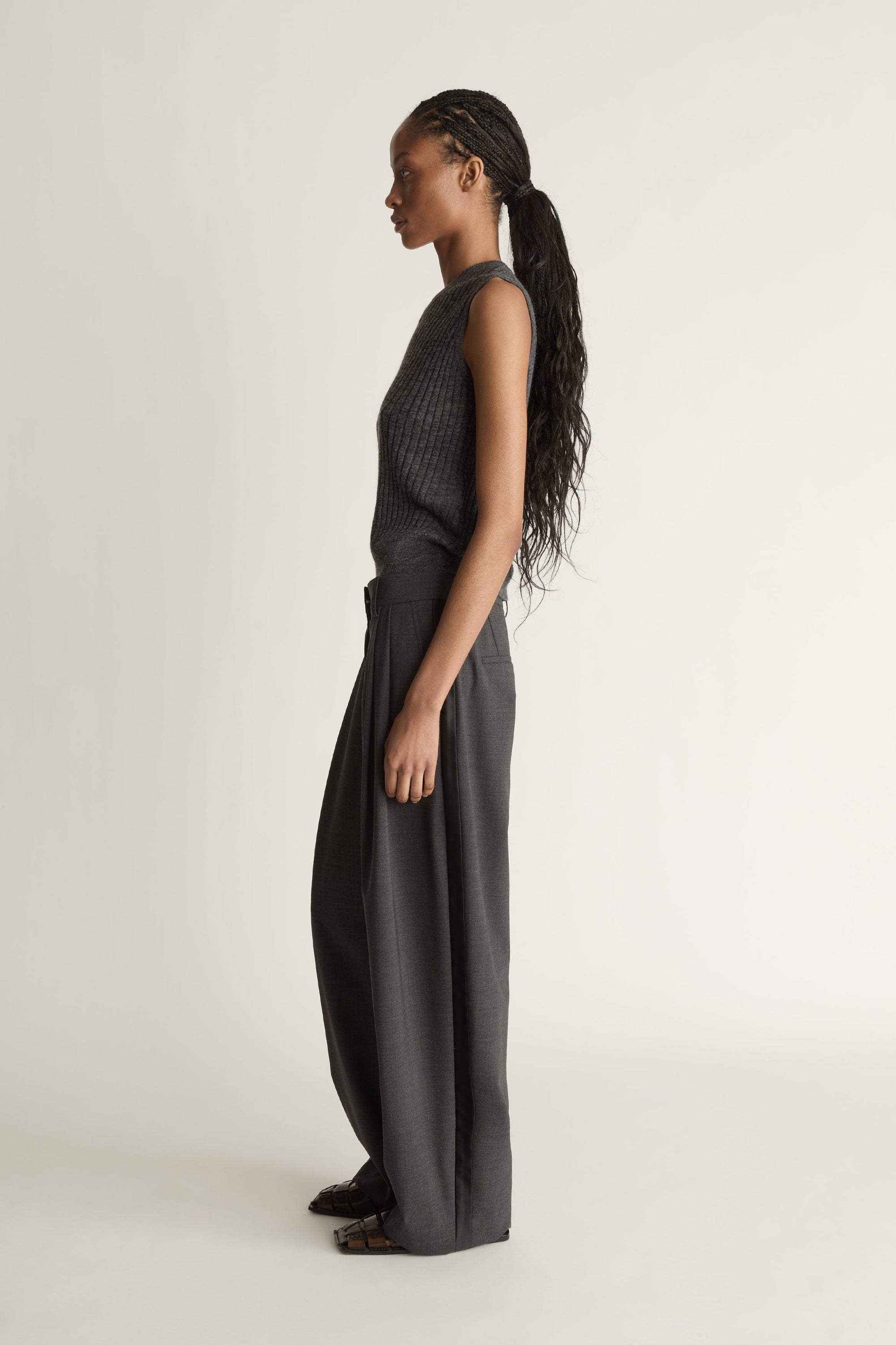 Woman wearing a sleeveless knitted top and wide-leg pants on a plain background