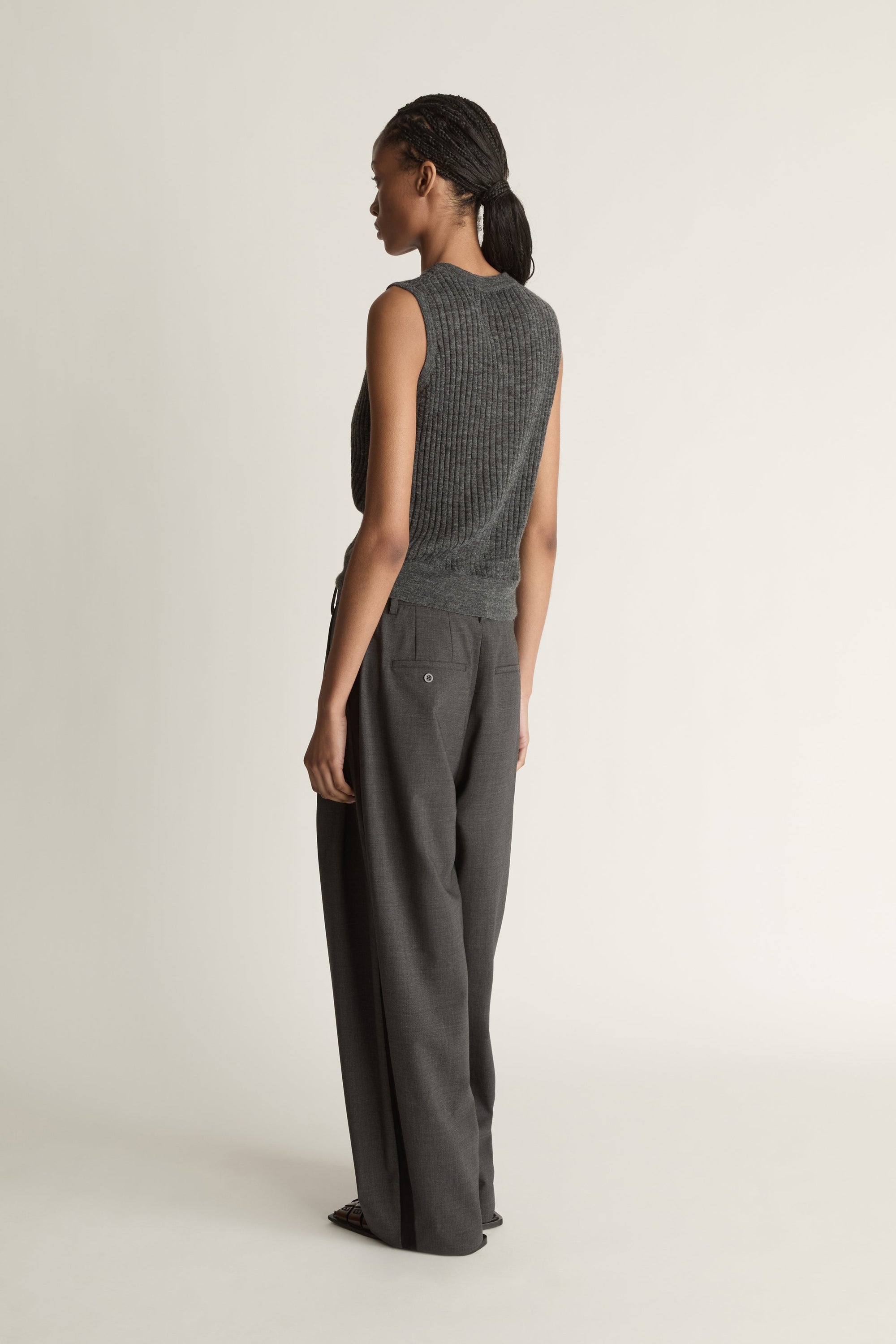 Woman wearing a sleeveless knitted top and wide-leg pants on a plain background