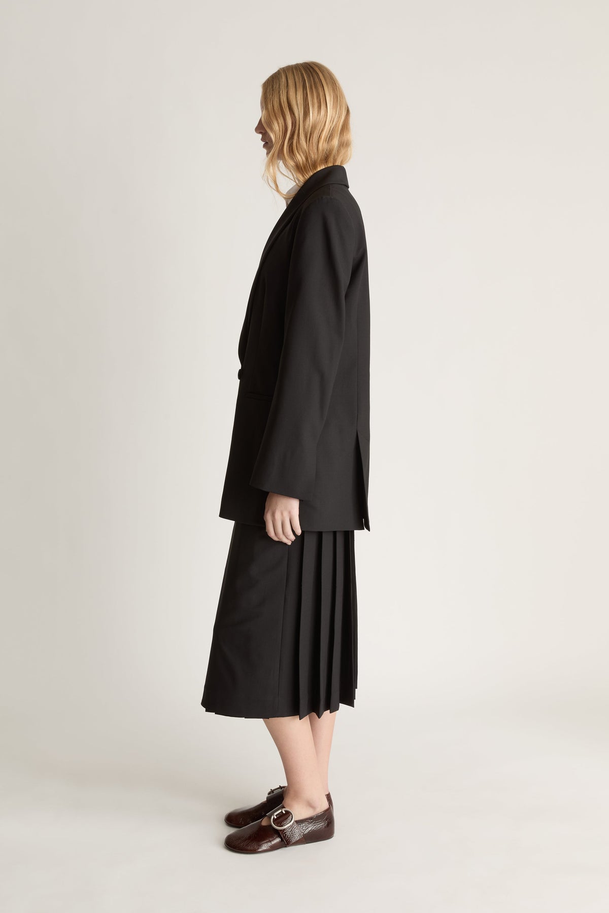 Side view of a person wearing a black coat and skirt on a plain background