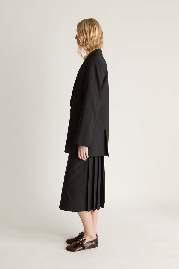 Side view of a person wearing a black coat and skirt on a plain background