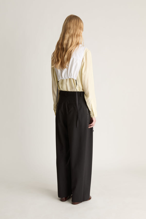 Back view of a p-erson wearing a white frill dickey over a yellow blouse and black pants on a plain background
