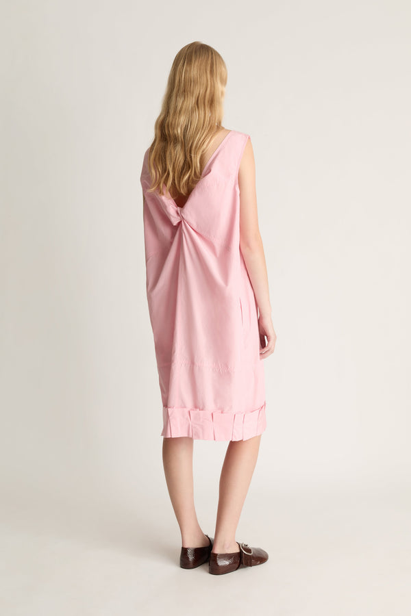 Woman wearing a pink dress with a twisted knot detail on the back against a white background