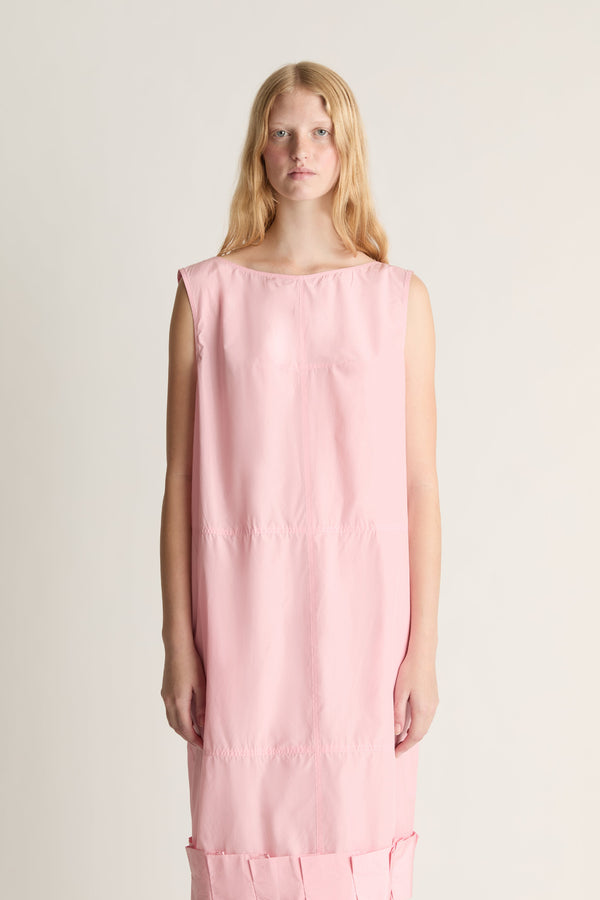 Close up of a woman wearing a sleeveless pink silk dress against a white studio background. 