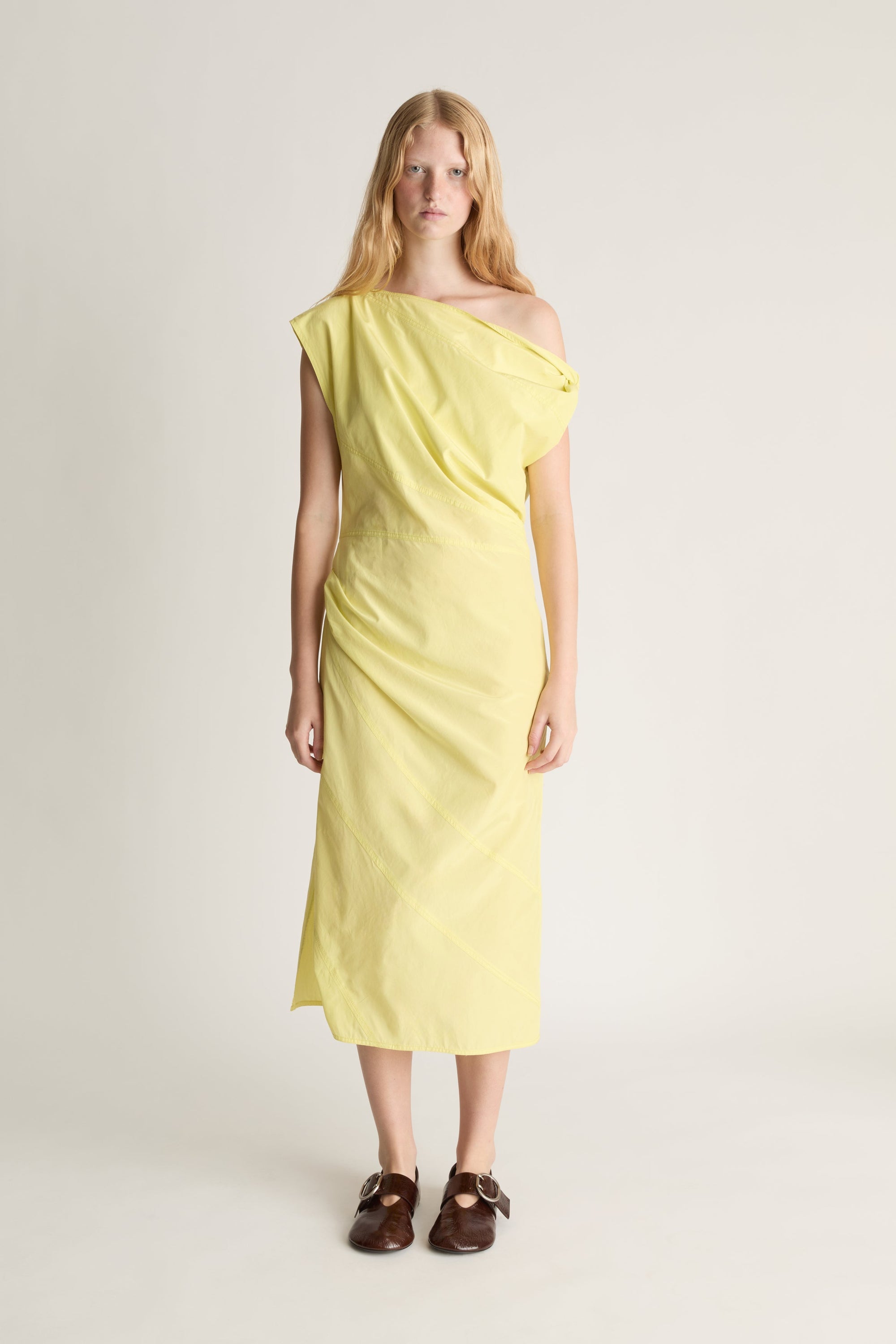 Front view of a woman wearing a yellow one-shoulder midi dress against a white studio background.