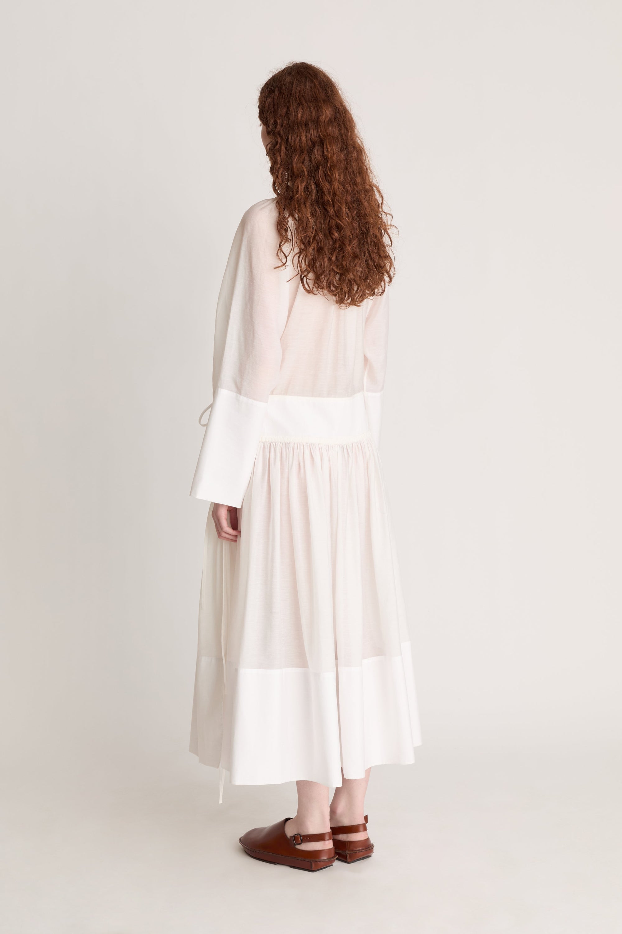 A woman wearing a long white dress with a tie detail, on a plain background
