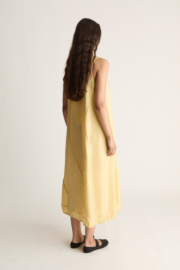 Back view of a woman with long wavy hair in a loose yellow sleeveless midi dress