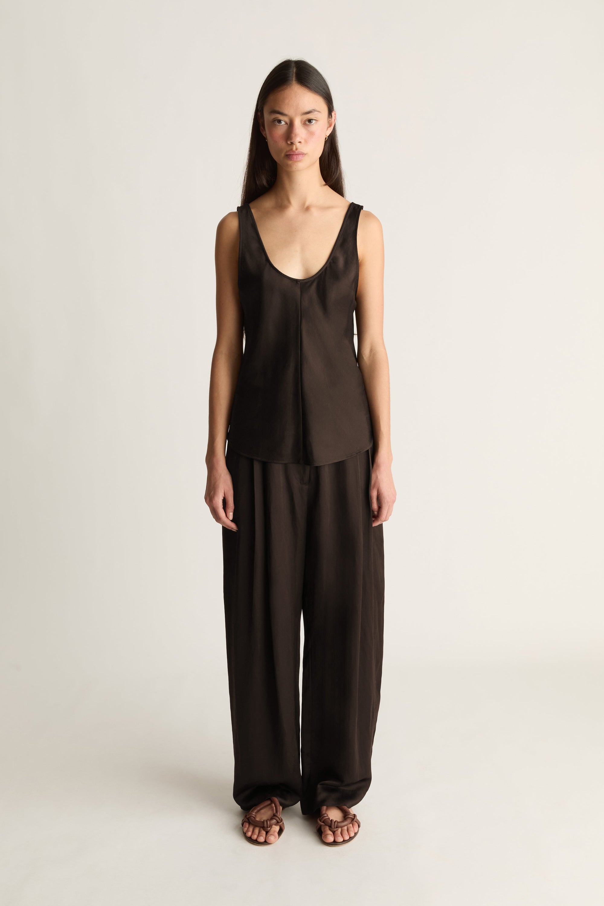 A woman modeling a dark brown sleeveless top and matching wide-leg pants set against a plain light gray studio background.