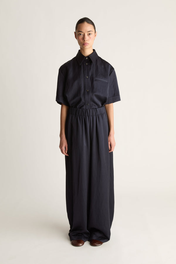Front view of a woman wearing a navy short-sleeved shirt and elasticated wide-leg trousers, shot against a white studio background.
