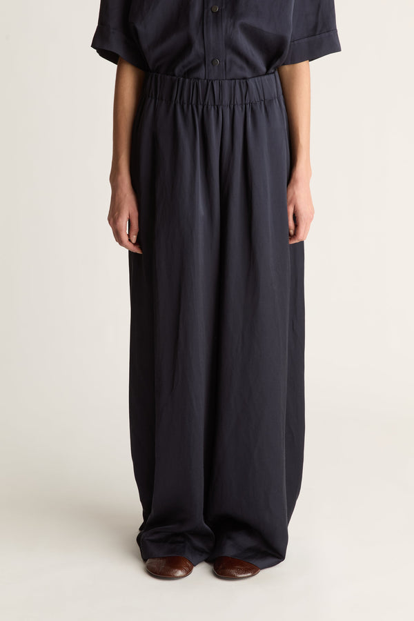 Close-up of a woman wearing a pair of wide-leg elasticated navy trousers, shot against a white studio background.