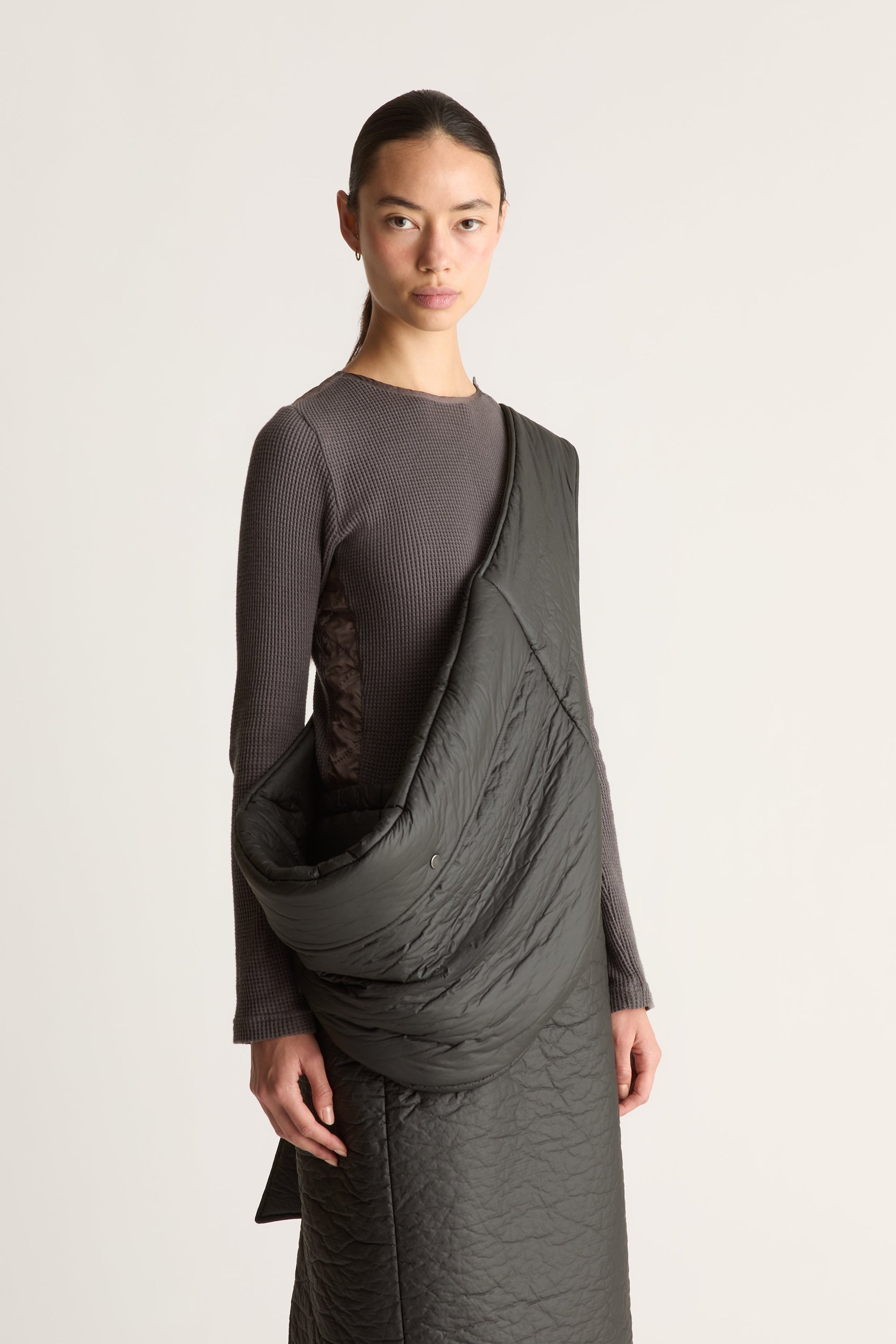 Close up of a model wearing a dark gray waffle knit long-sleeve top and skirt, photographed against a plain light gray studio background.
