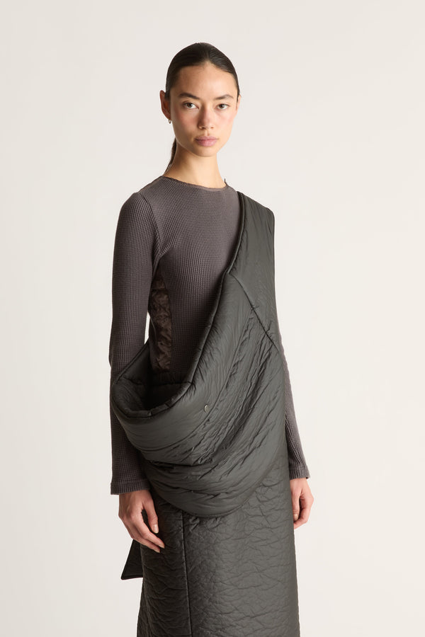 Close up of a model wearing a dark gray waffle knit long-sleeve top and skirt, photographed against a plain light gray studio background.
