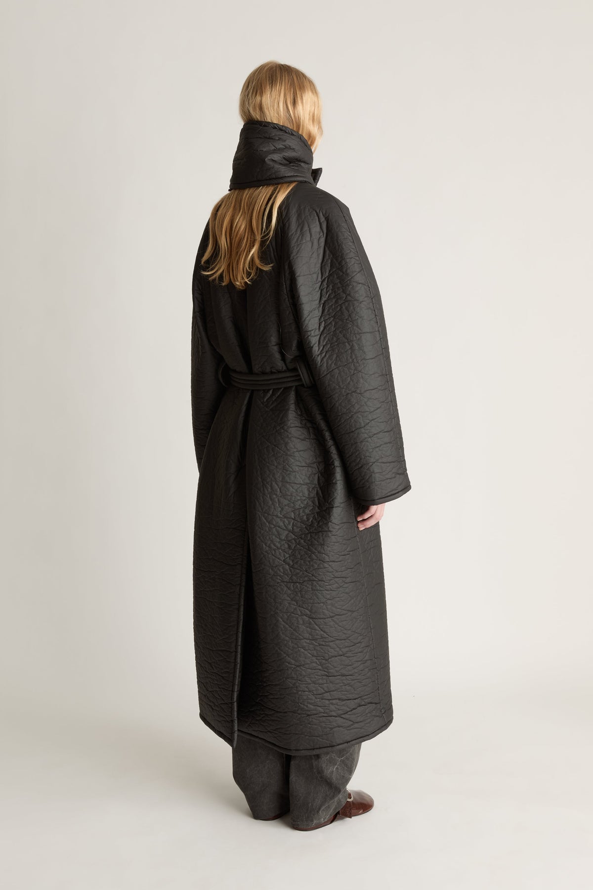 Back view of a person wearing a long dark coat agaist a white studio background