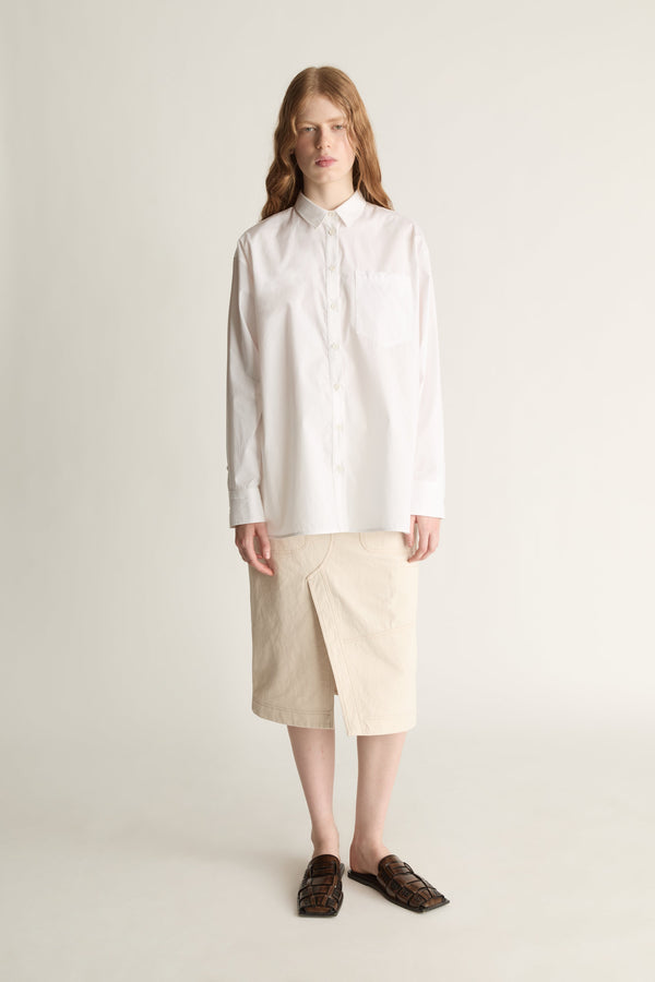 Person wearing a white shirt and beige skirt on a plain background