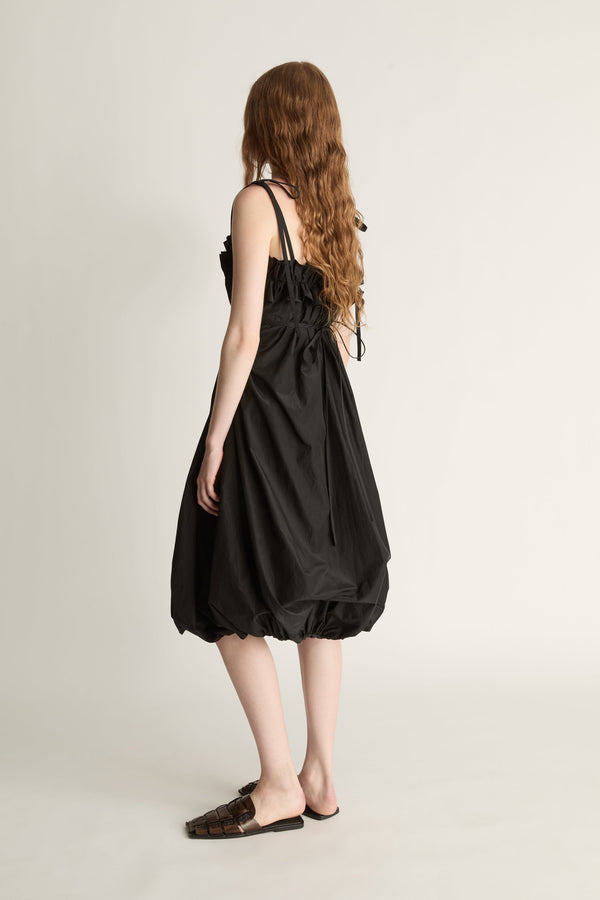 Back view image of a woman wearing a black bubble-style midi dress and brown shoes against a white studio background.