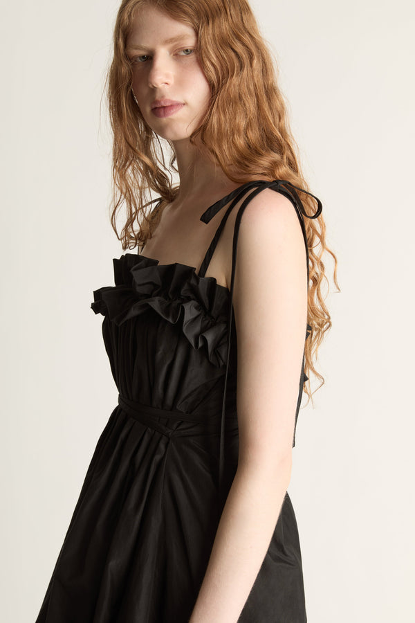 Close up of a woman wearing a black dress with ruffled details on a plain background