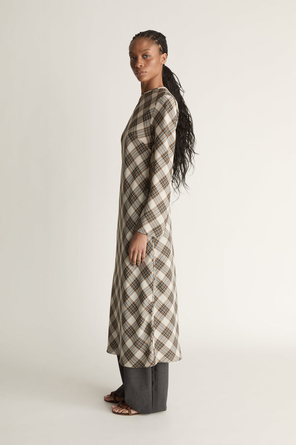Side view of a woman wearing a long- sleeve midi length plaid dress on a white background