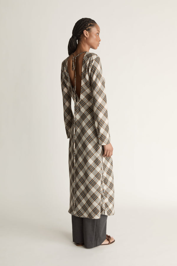 Back view image of a woman wearing a long plaid scoop-back midi dress against a white studio background.