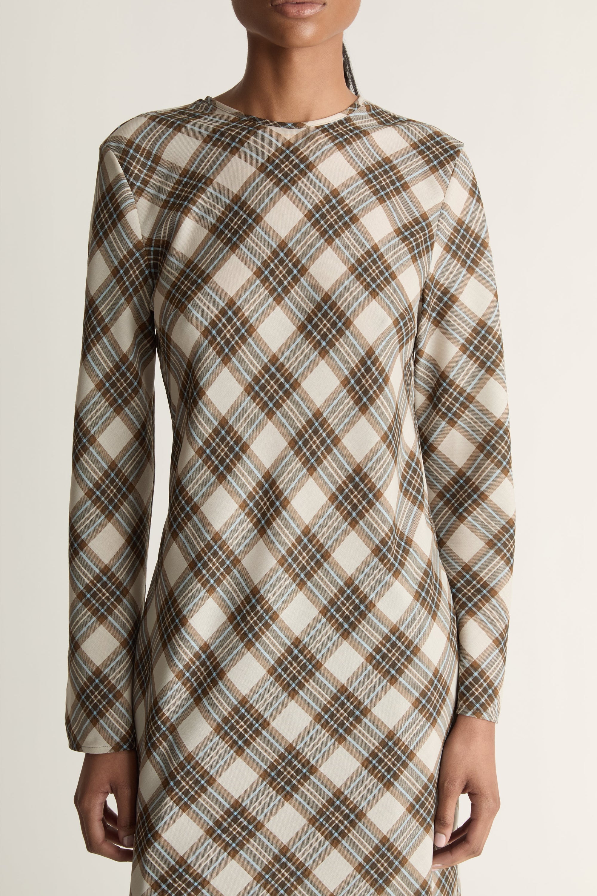 Close up of a woman wearing a long sleeve plaid dress against a studio background