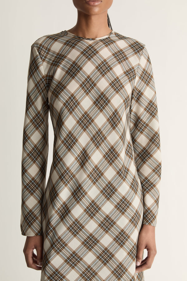 Close up of a woman wearing a long sleeve plaid dress against a studio background