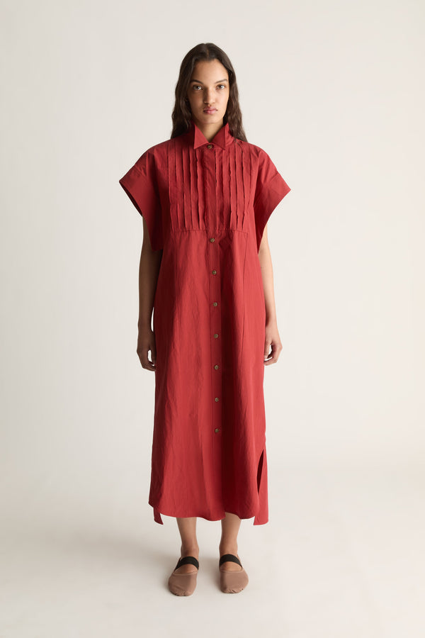 Front view of a woman wearing a red short-sleeve midi shirt dress with pleated bib and tan flats against a white studio background