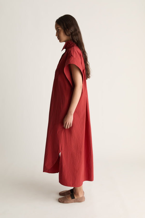 Side view of a woman in a red midi shirt dress with cap sleeve and curved hem