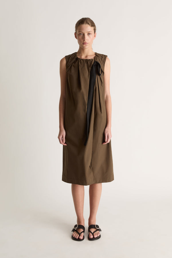 Front view of a woman wearing a khaki sleeveless midi dress with black ribbon tie against a white studio background