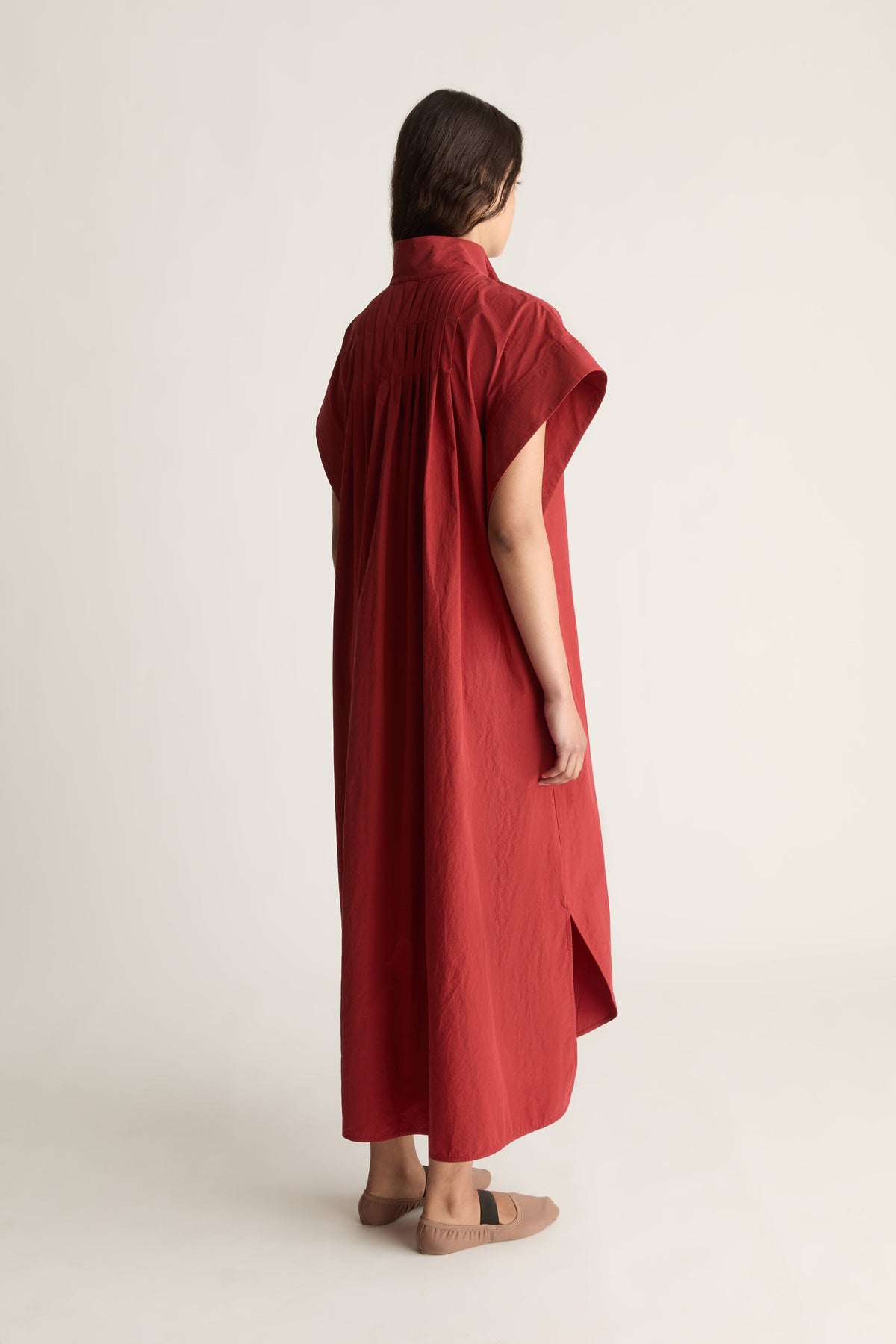 Back view of a woman in an oversized red shirt dress with back pleat and side slits