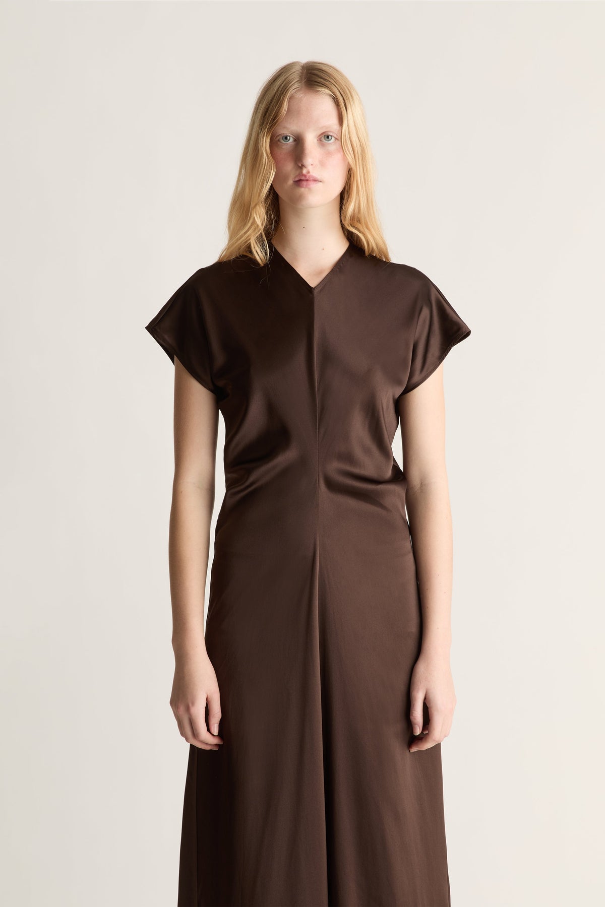 Close up of a woman wearing a brown silk short sleeve dresss against a white studio background.