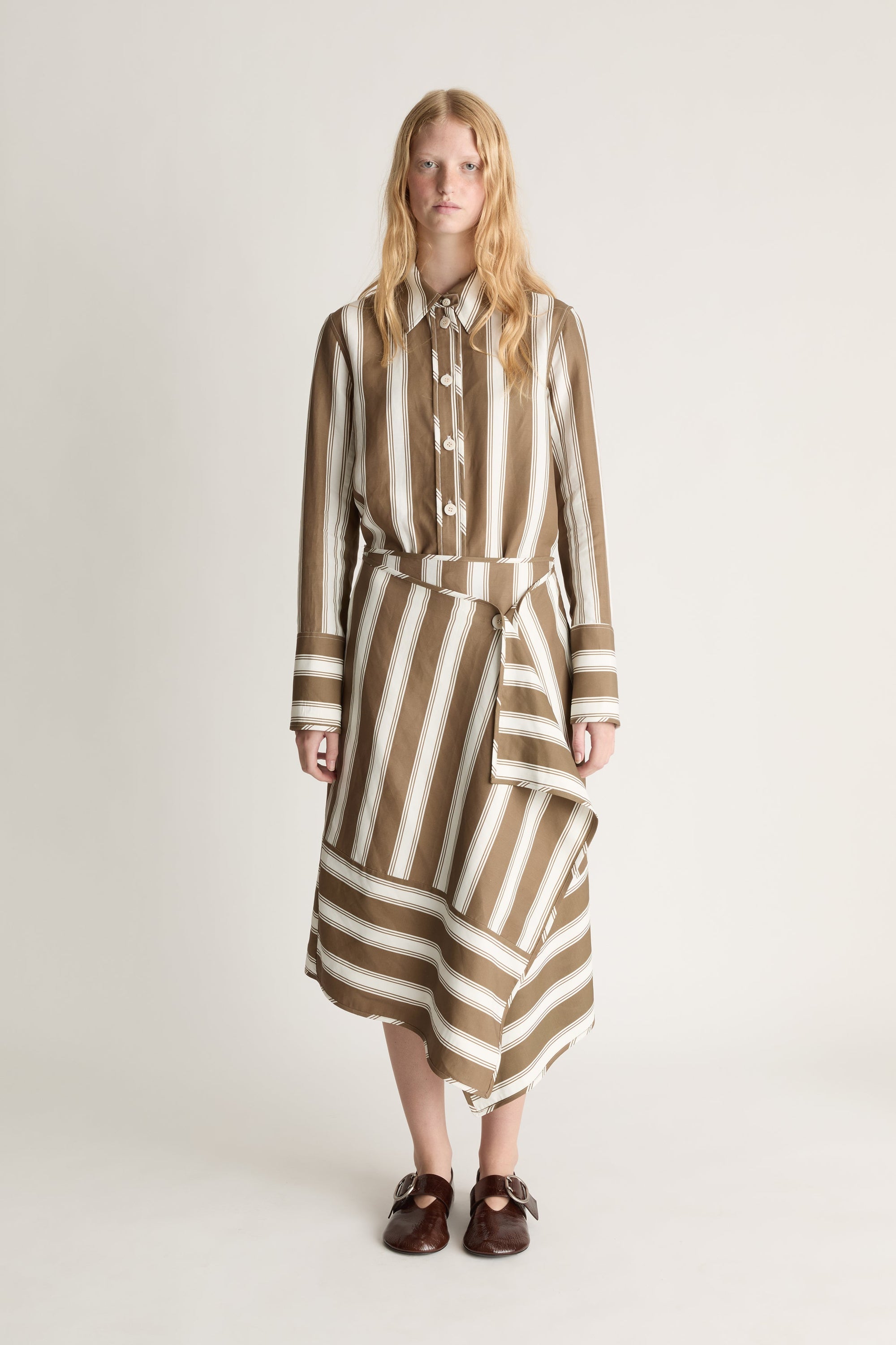 Front view of a woman wearing a brown and white shirt and matching wrap skirt  on a plain background