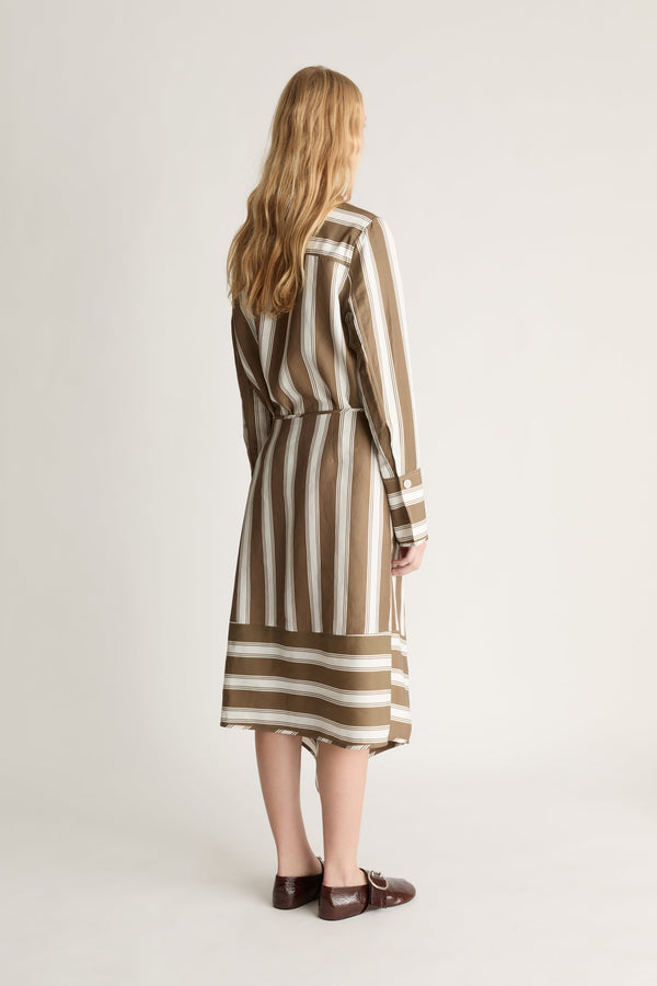 Back view of a woman wearing a brown and white striped button up shirt and skirt against a white background. 