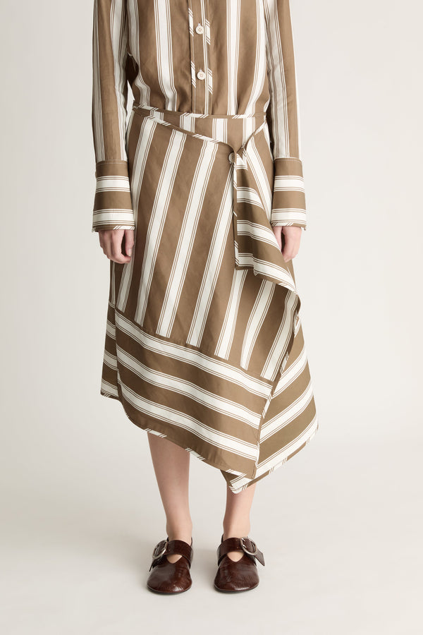 Close up view of a woman wearing a striped brown and white button-up shirt and matching wrap skirt shot against a white studio background. 
